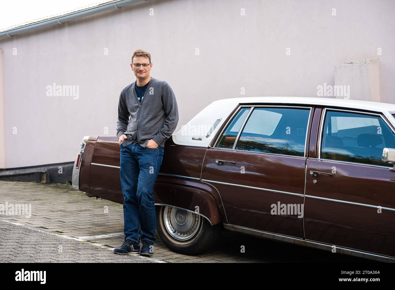 Koekelberg, région de Bruxelles-capitale, Belgique, 23 septembre 2023 - 44 yo homme blanc penchant agaisnt une vieille minuterie Cadillac Sedan de ville Banque D'Images