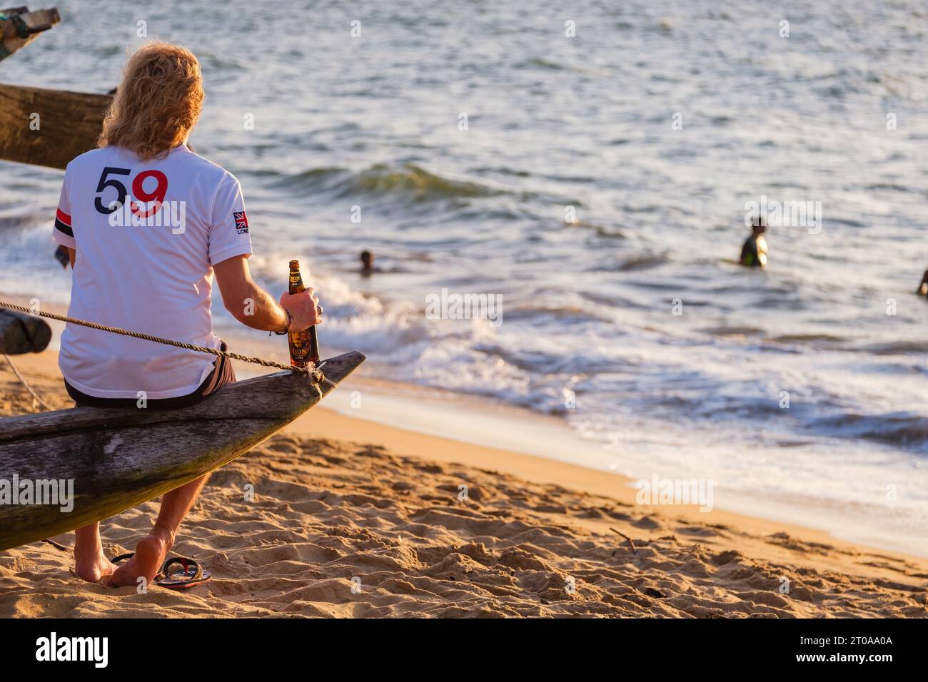 Touriste buvant une bière Lion assis sur un bateau de pêcheur sur la plage de Negombo au Sri Lanka au coucher du soleil Banque D'Images
