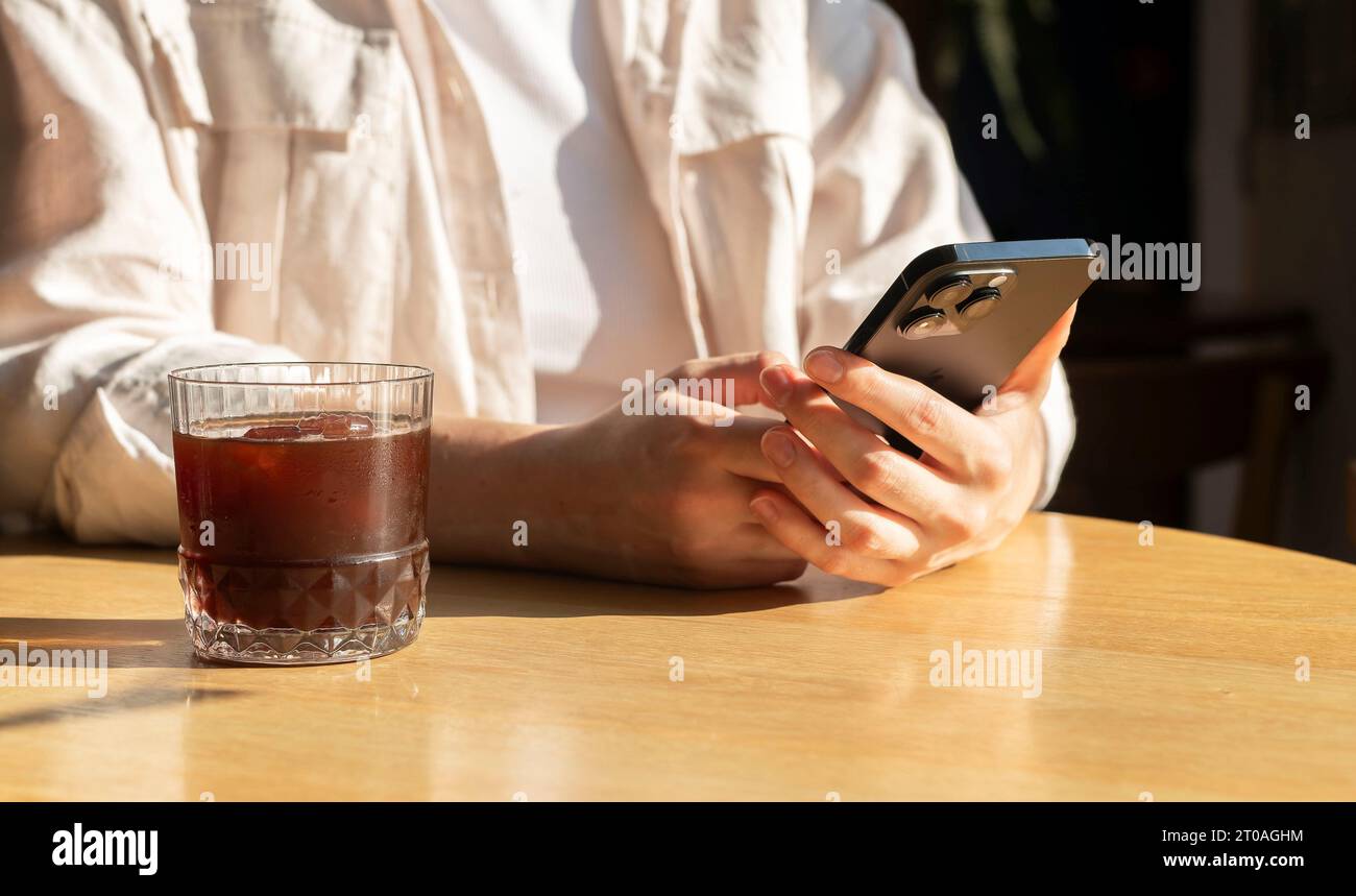 Berlin, Allemagne septembre 16 2023 mains avec smartphone, lire des nouvelles, faire défiler des messages, nourrir à la table de café avec verre à café Banque D'Images