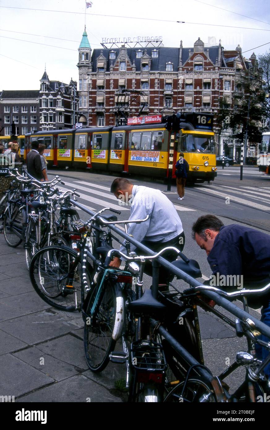 Scène de rue avec peole verrouillant leurs vélos alors qu'une voiture de rue approche à Amsterdam, en Hollande Banque D'Images