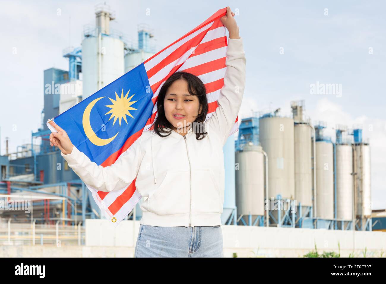 Jeune femme heureuse avec drapeau de la Malaisie contre fond d'usine Banque D'Images