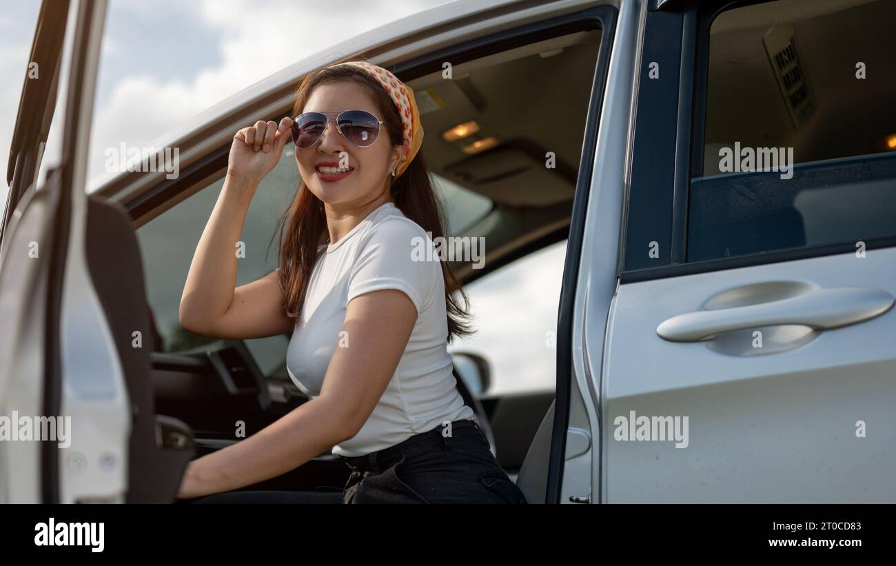 Une belle femme asiatique millénaire en lunettes de soleil sort de la voiture après être arrivée à destination. Road trip, vacances d'été, voyages Banque D'Images