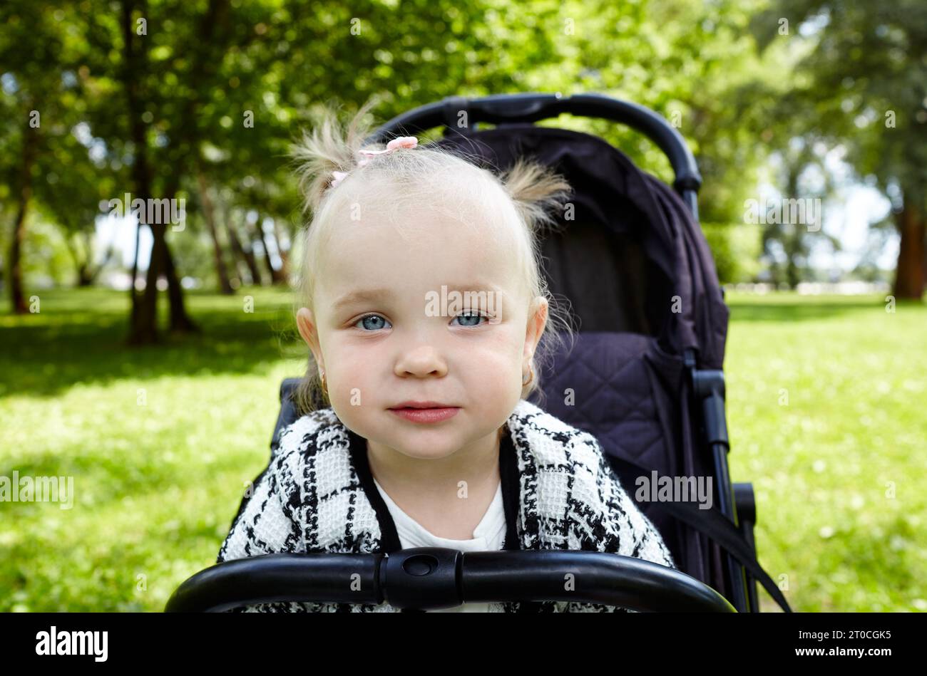 Bébé en poussette sur une promenade dans le parc d'été. Adorable petite fille assise dans une poussette, expression faciale drôle. Enfant en buggy Banque D'Images