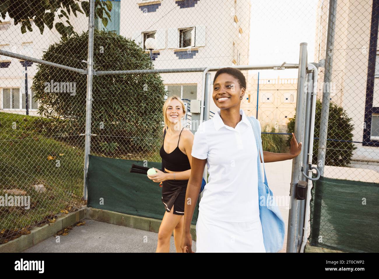 Deux jeunes amis entrant sur un court de tennis pour un match. Jeunes femmes gaies en vêtements de tennis arrivant à un court de tennis pour un jeu amateur. Banque D'Images