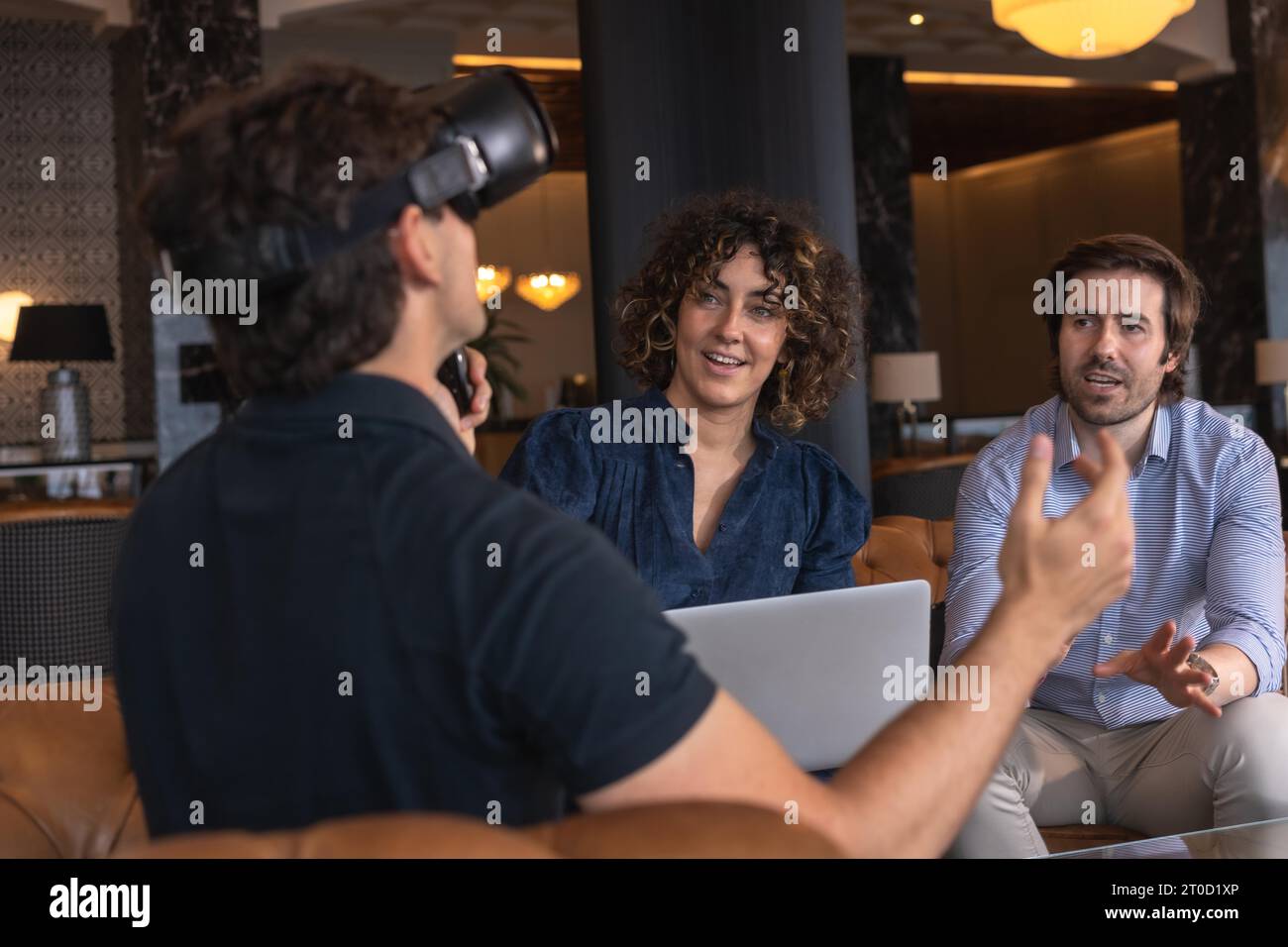 Femme d'affaires à l'aide d'un ordinateur portable avec un collègue gesturant en portant un simulateur de réalité virtuelle Banque D'Images