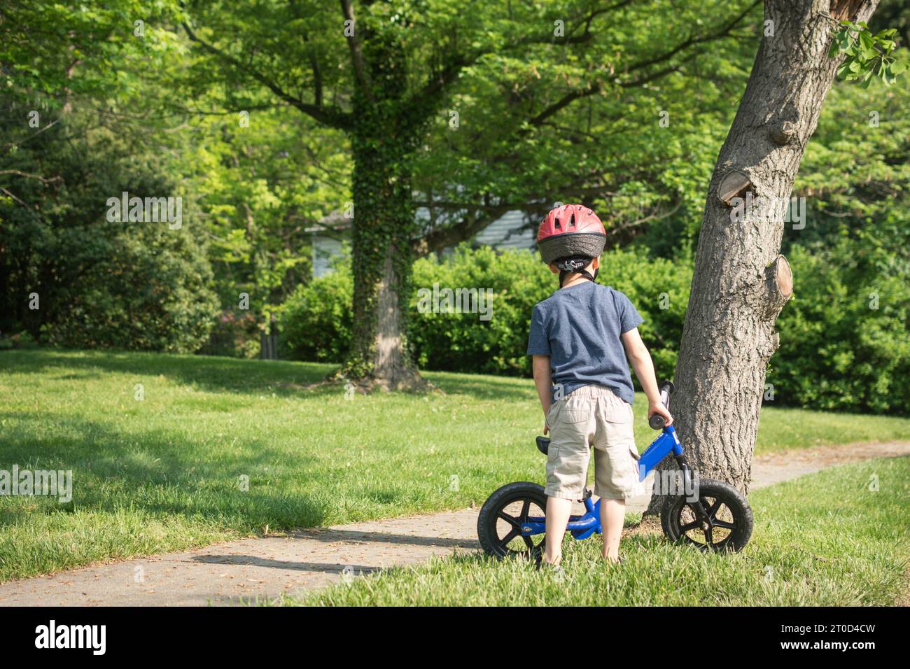 Jeune garçon se préparant à monter le vélo d'équilibre sur le trottoir de banlieue. Banque D'Images