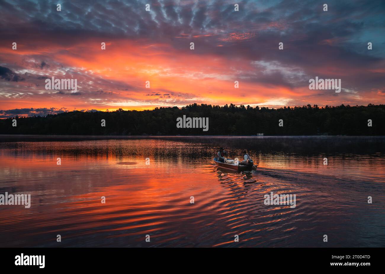Deux personnes dans un bateau de pêche se dirigeant à travers un lac au lever du soleil. Banque D'Images