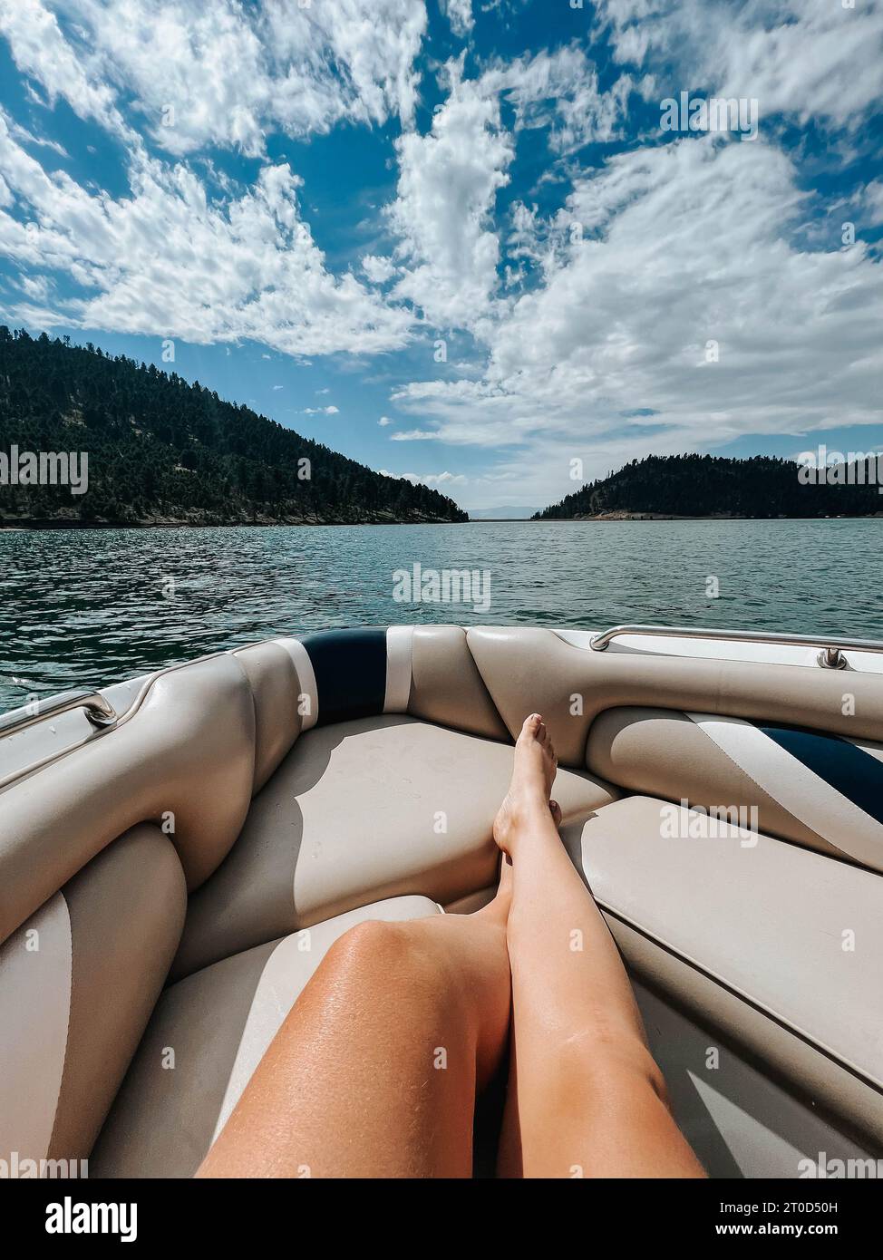 pieds de femme se détendant sur un bateau au milieu du paysage serein du lac de montagne. Banque D'Images