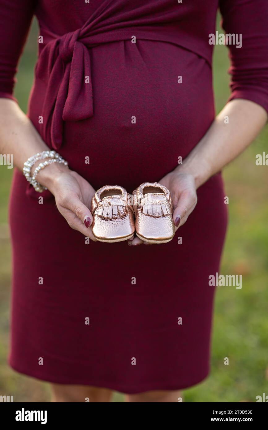 Femme enceinte tenant une paire de chaussures de bébé devant son ventre Banque D'Images