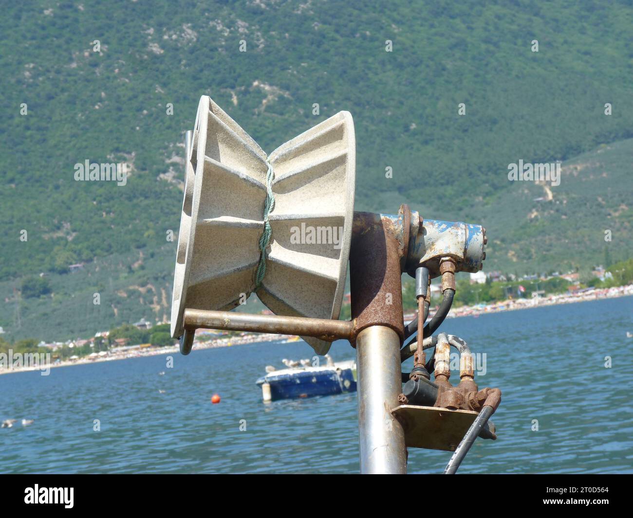 Grand haut-parleur conique blanc monté sur un poteau en métal près du plan d'eau calme avec des bateaux et Green Hills en arrière-plan Banque D'Images