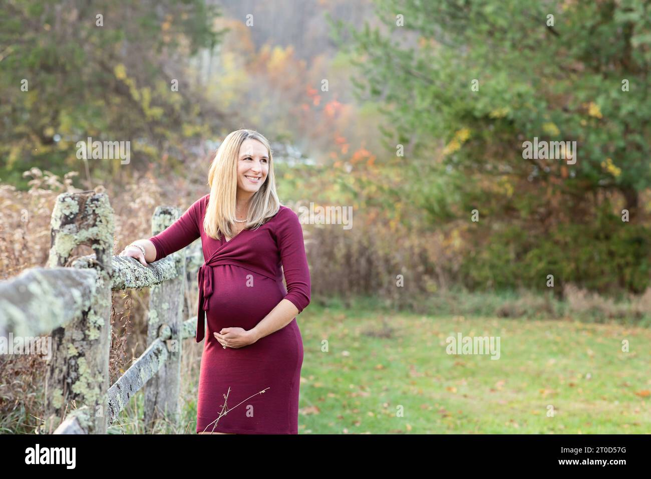 Femme enceinte tenant son ventre debout dans un champ à côté d'une clôture Banque D'Images