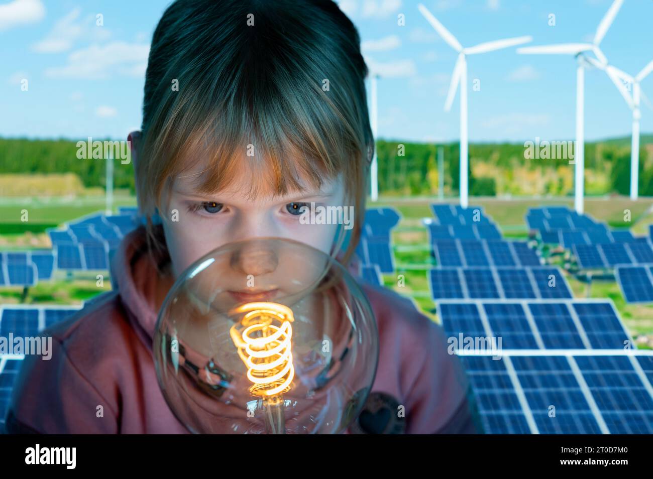 Symbole pour l'utilisation d'énergies renouvelables. L'enfant regarde une ampoule devant l'énergie éolienne et les panneaux solaires. Banque D'Images