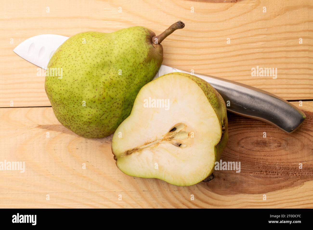 Deux moitiés d'une poire verte biologique avec un couteau en métal, gros plan, sur une table en bois, vue de dessus. Banque D'Images