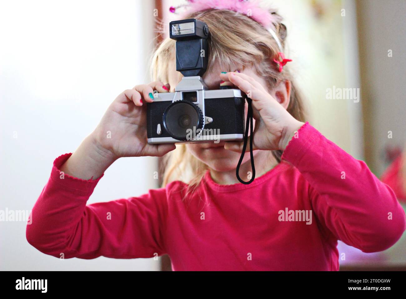 Une jeune femme vêtue d'une tenue rose vibrante se tient contre un mur, tenant avec confiance un appareil photo alors qu'elle capture sa propre vision créative Banque D'Images