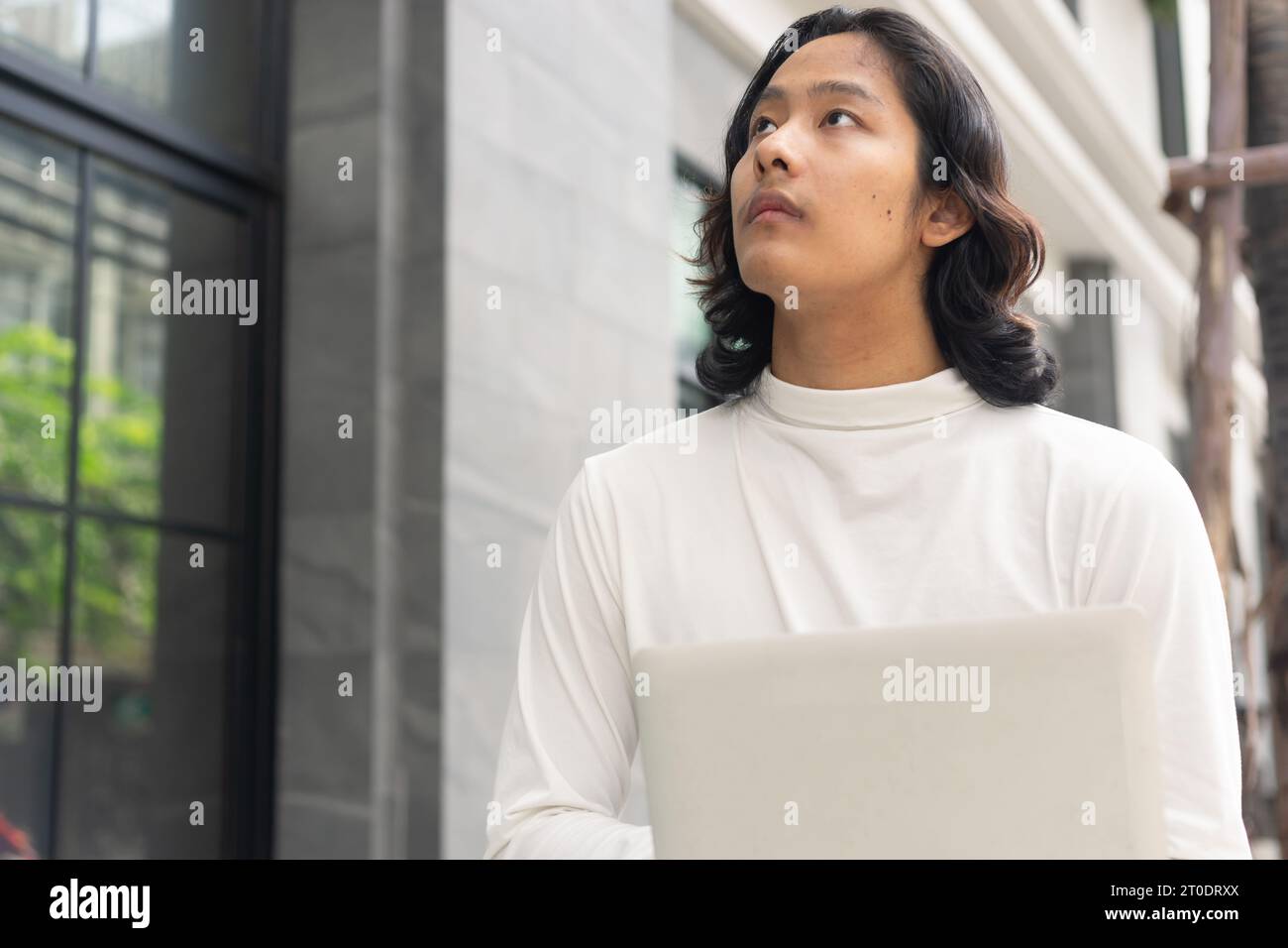 Jeune homme d'affaires asiatique utilisant un ordinateur portable à proximité de son espace de travail de bureau contre des bâtiments d'entreprise contemporains dans la ville. Banque D'Images