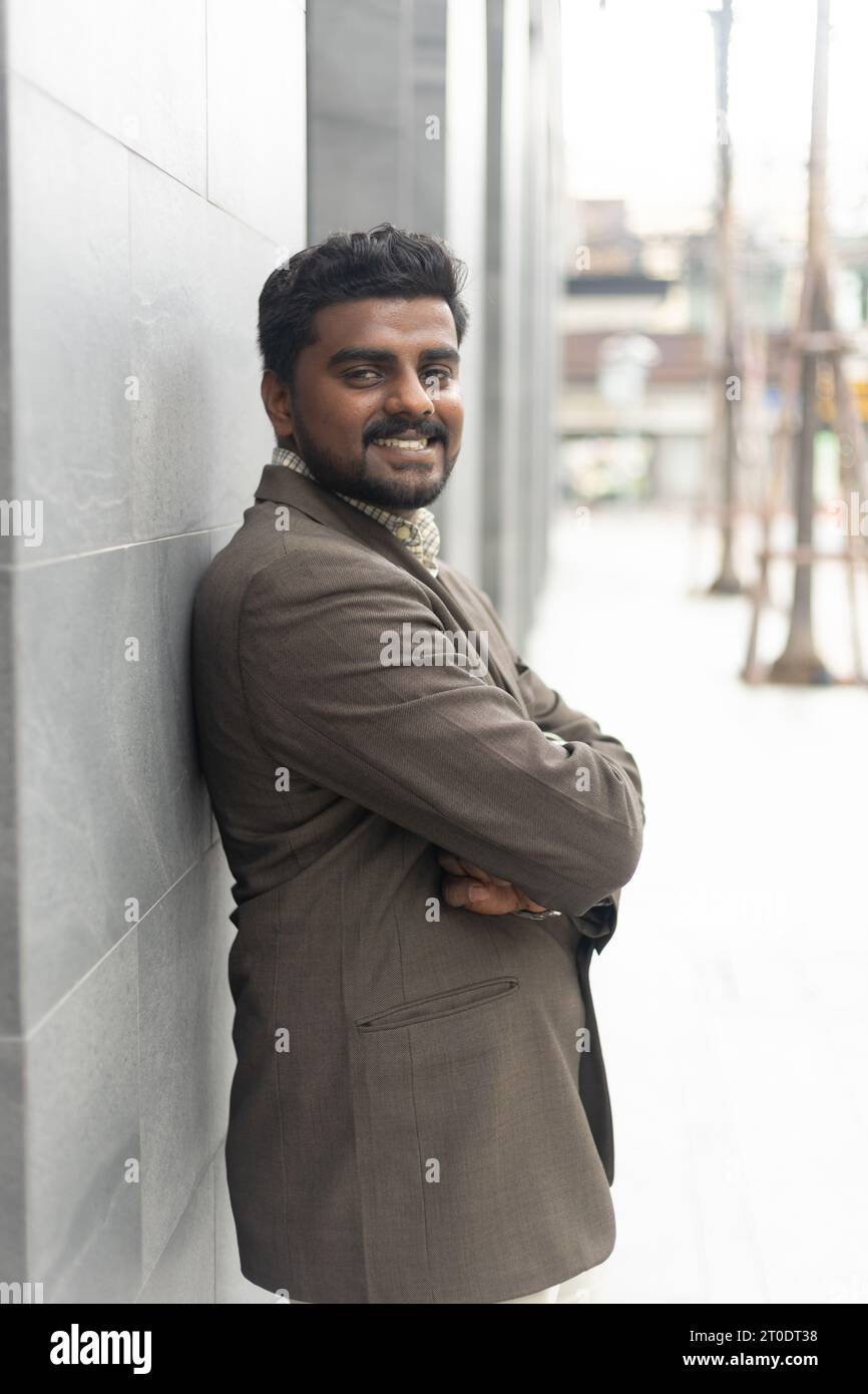 Jeune homme d'affaires indien souriant portrait sur le chemin de son bureau contre les bâtiments d'entreprise contemporains dans la ville. Banque D'Images