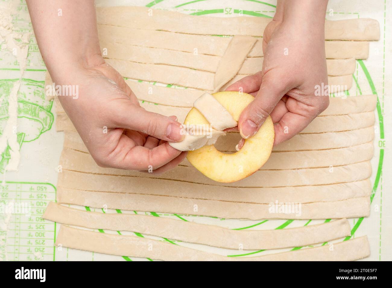 Les mains d'une femme enveloppent un anneau de pommes avec une bande de pâte feuilletée pour la cuisson au four. Cuisine maison. Banque D'Images