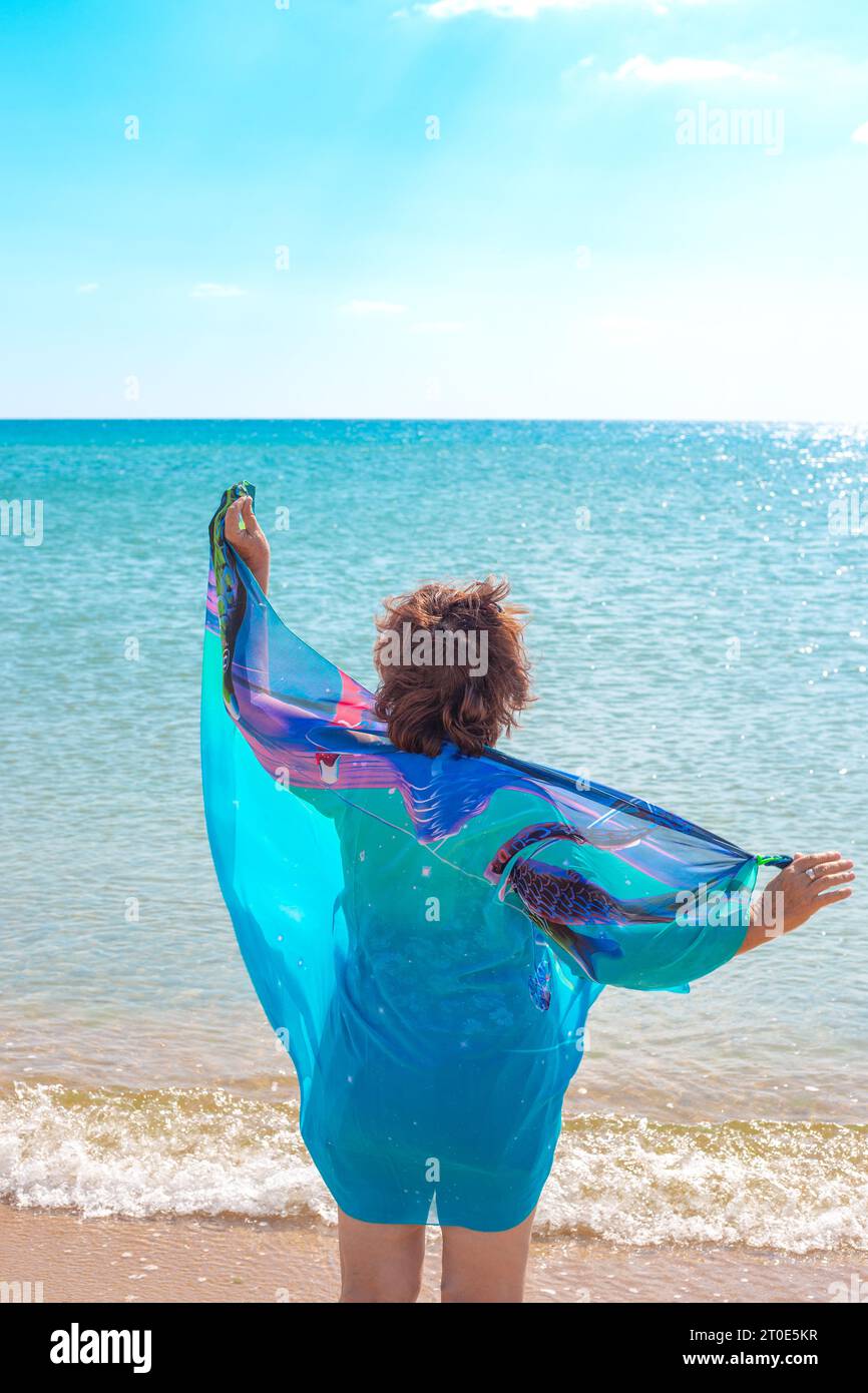 Une dame en maillot de bain et un paréo bleu repose sur le bord de la mer un jour d'été. Banque D'Images
