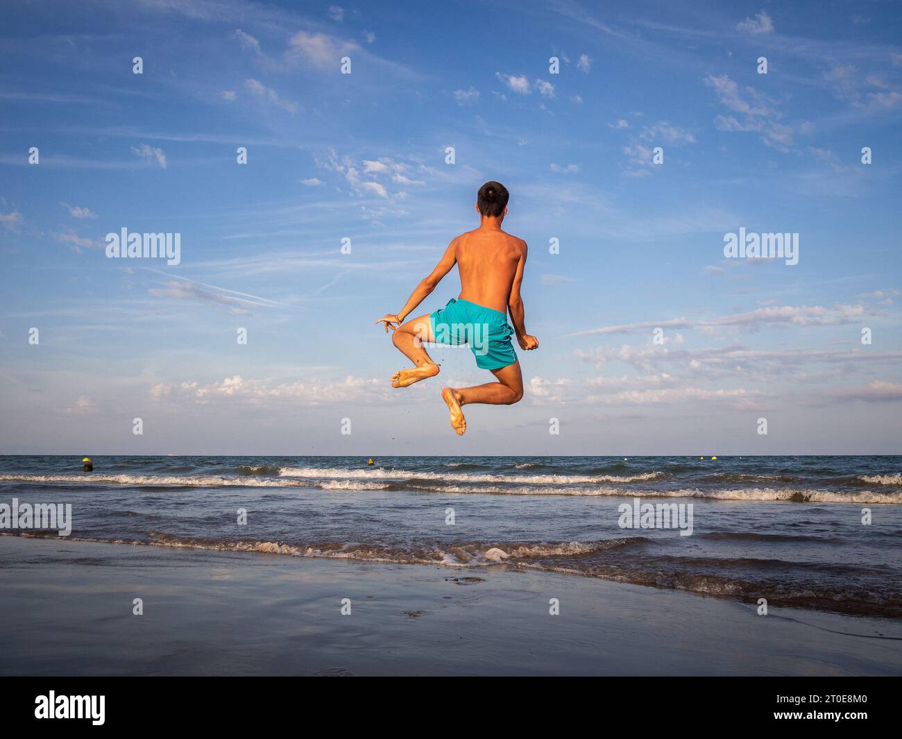 Garçon de derrière sautant joyeusement sur le bord de la mer Banque D'Images