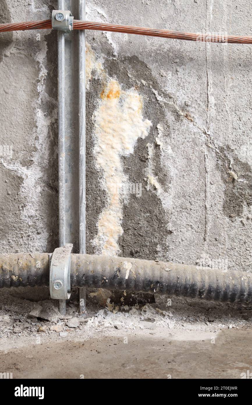 Gros plan d'une fuite d'eau active dans le mur de la salle électronique ou du sous-sol. Mouiller les taches sombres avec une tache blanche et une efflorescence au-dessus du grand câble électrique. Banque D'Images