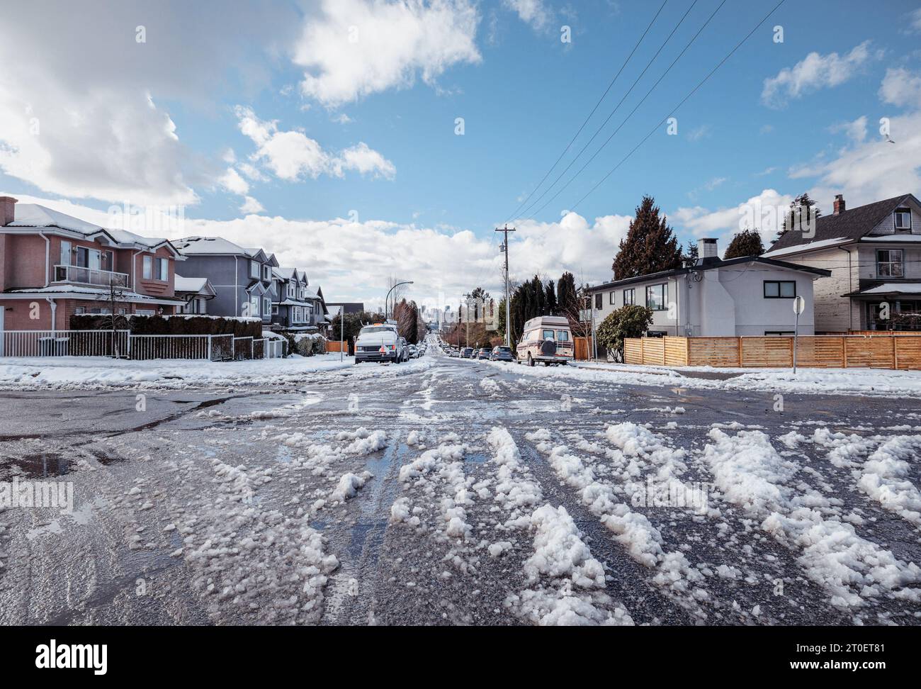 Rue résidentielle glissante après une tempête de neige ou une explosion arctique. Journée ensoleillée avec grande fonte vers le bas sur la rue latérale non labourée avec des voitures garées. East Vancouver avec Banque D'Images