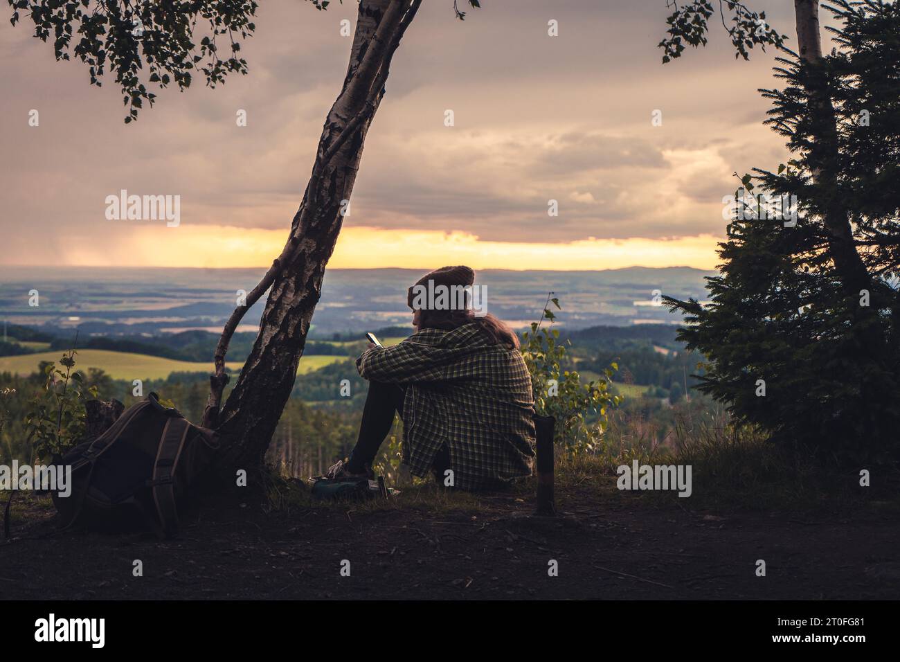 Une fille assise sur le dessus de la monture et profitant du coucher de soleil jaune. Femme de randonnée en chemise se relaxant sur la falaise en regardant un beau landsc ensoleillé Banque D'Images