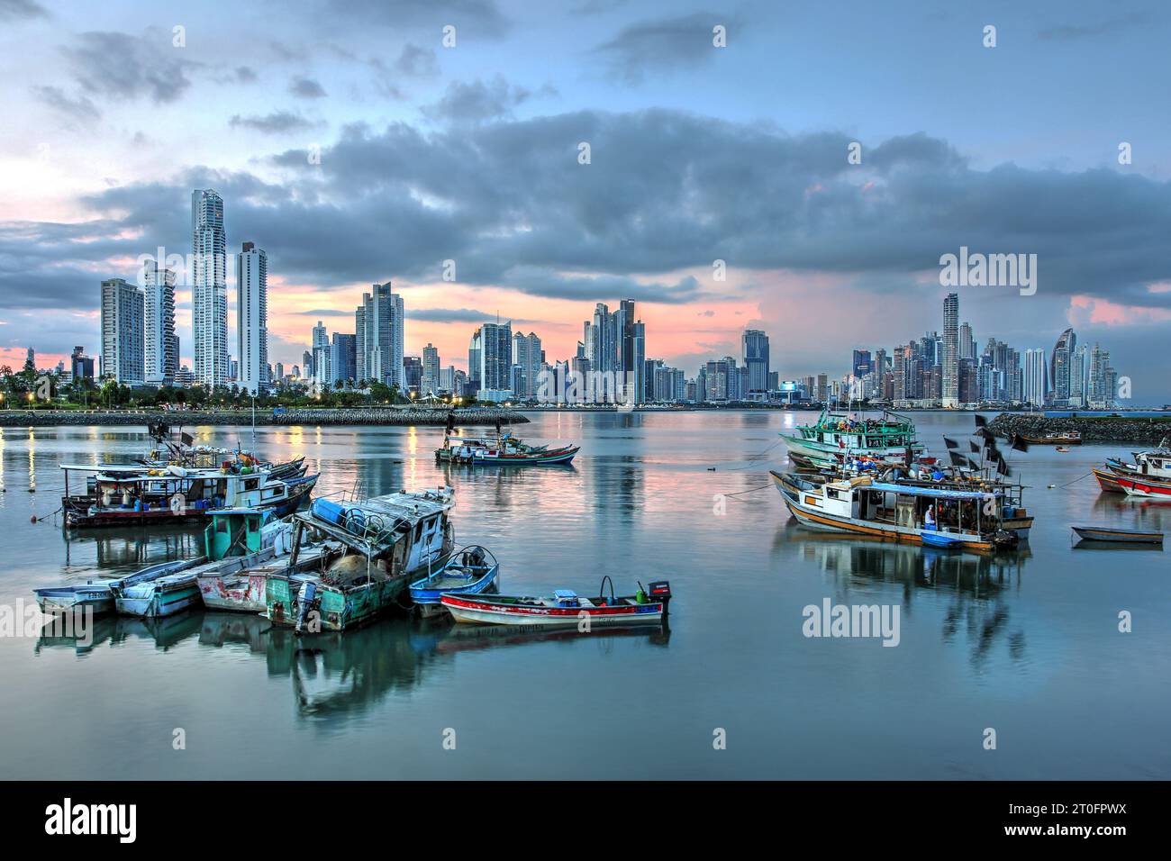 Skyline futuriste de la ville de Panama au coucher du soleil avec des bateaux de pêche au premier plan reflétant dans l'eau calme. Banque D'Images