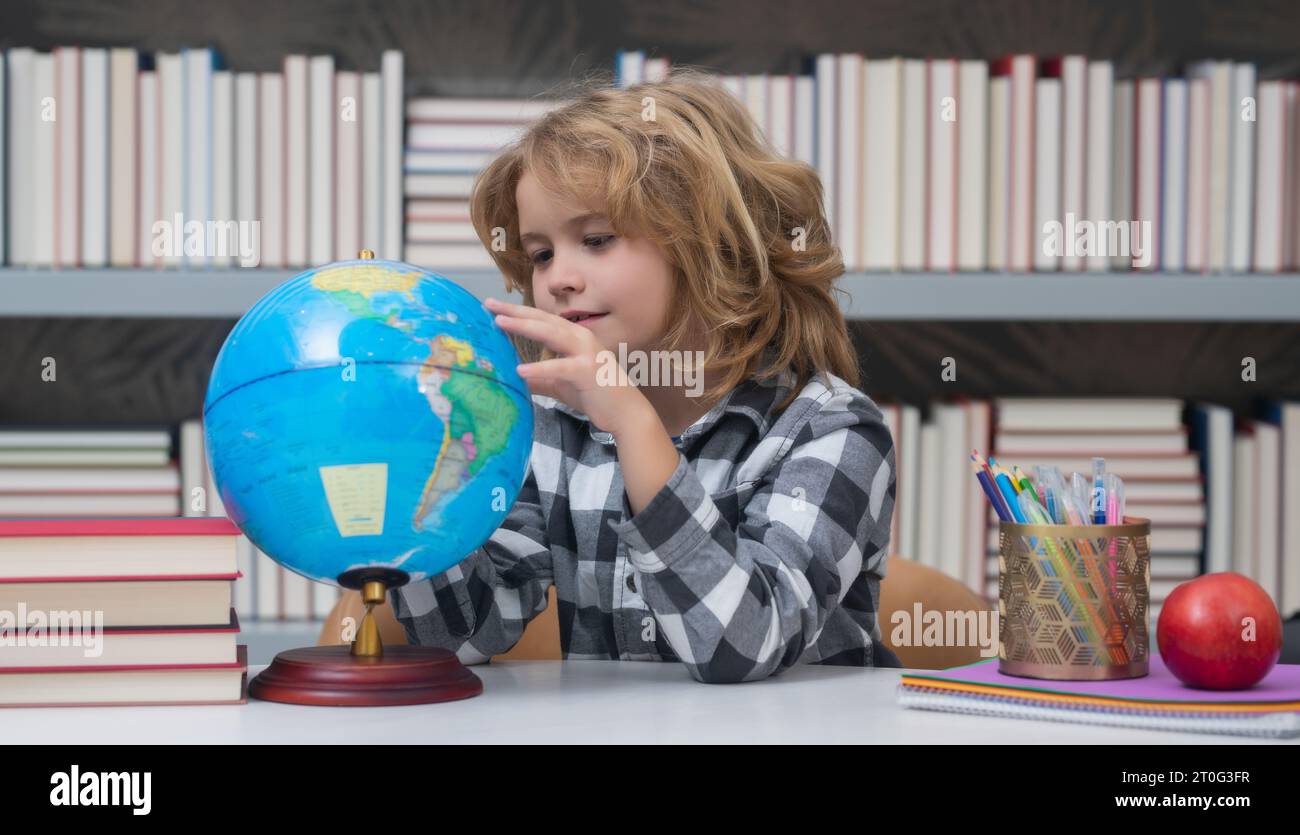 Élève regardant globe dans la bibliothèque à l'école élémentaire. Globe terrestre. Enfant garçon de l'école primaire avec livre. Concept d'éducation et lea Banque D'Images