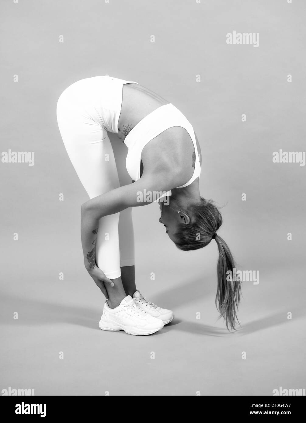 Tout le corps de jeune femme souriante gaie dans les vêtements de sport étirant, isolé sur fond gris. Bonne santé belle sportswoman. Banque D'Images