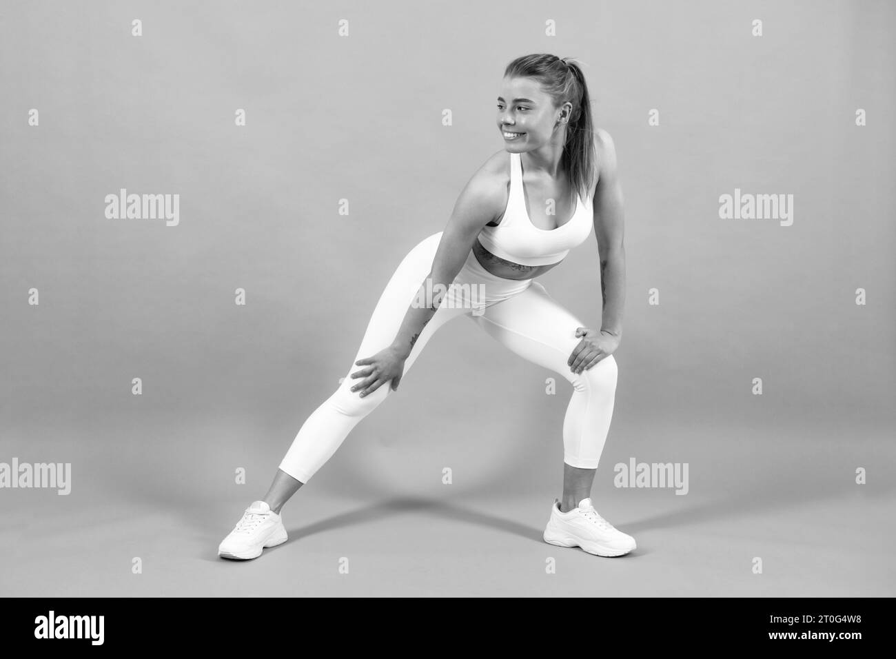 Femme sportive en stretching. Vêtements de sport, vêtements de sport. Jeune magnifique modèle s'étendant avant l'entraînement sur le studio gris Banque D'Images