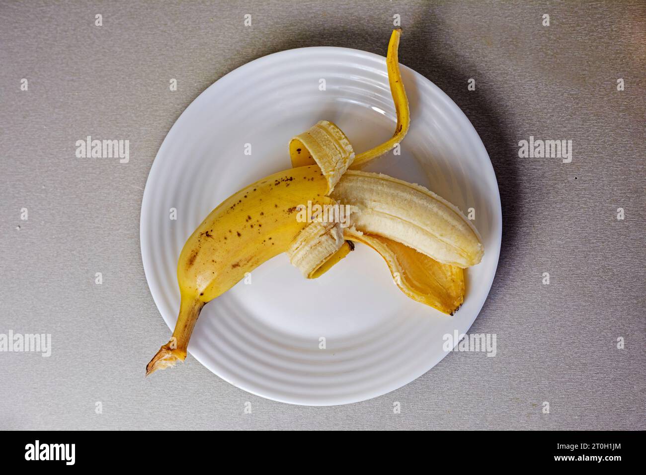 banane pelée sur une assiette blanche sur une table grise. petit déjeuner, snack Banque D'Images