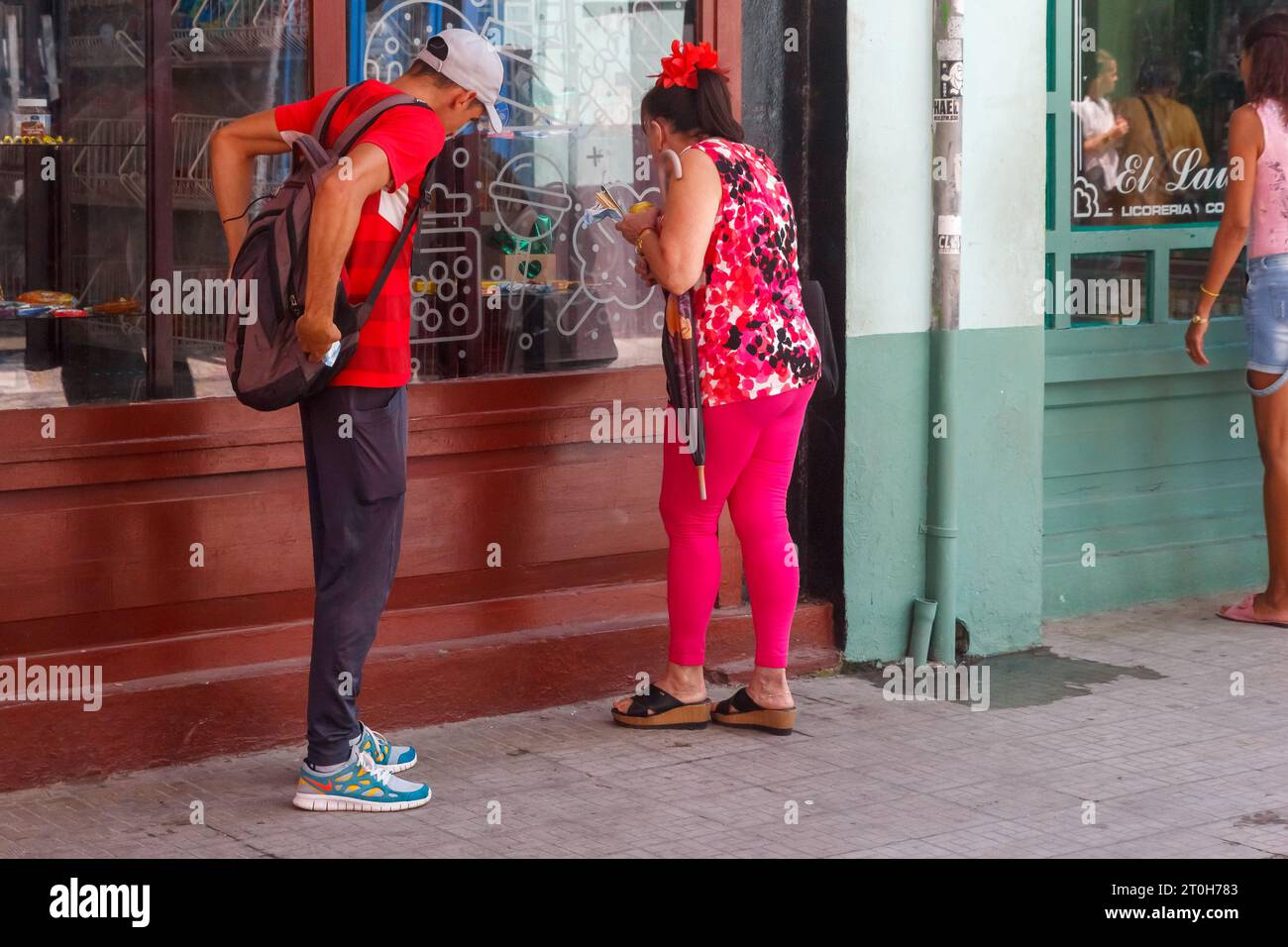 La Havane, Cuba - 29 septembre 2023 : une cubaine regarde dans une vitrine de magasin. Un homme attend à ses côtés Banque D'Images