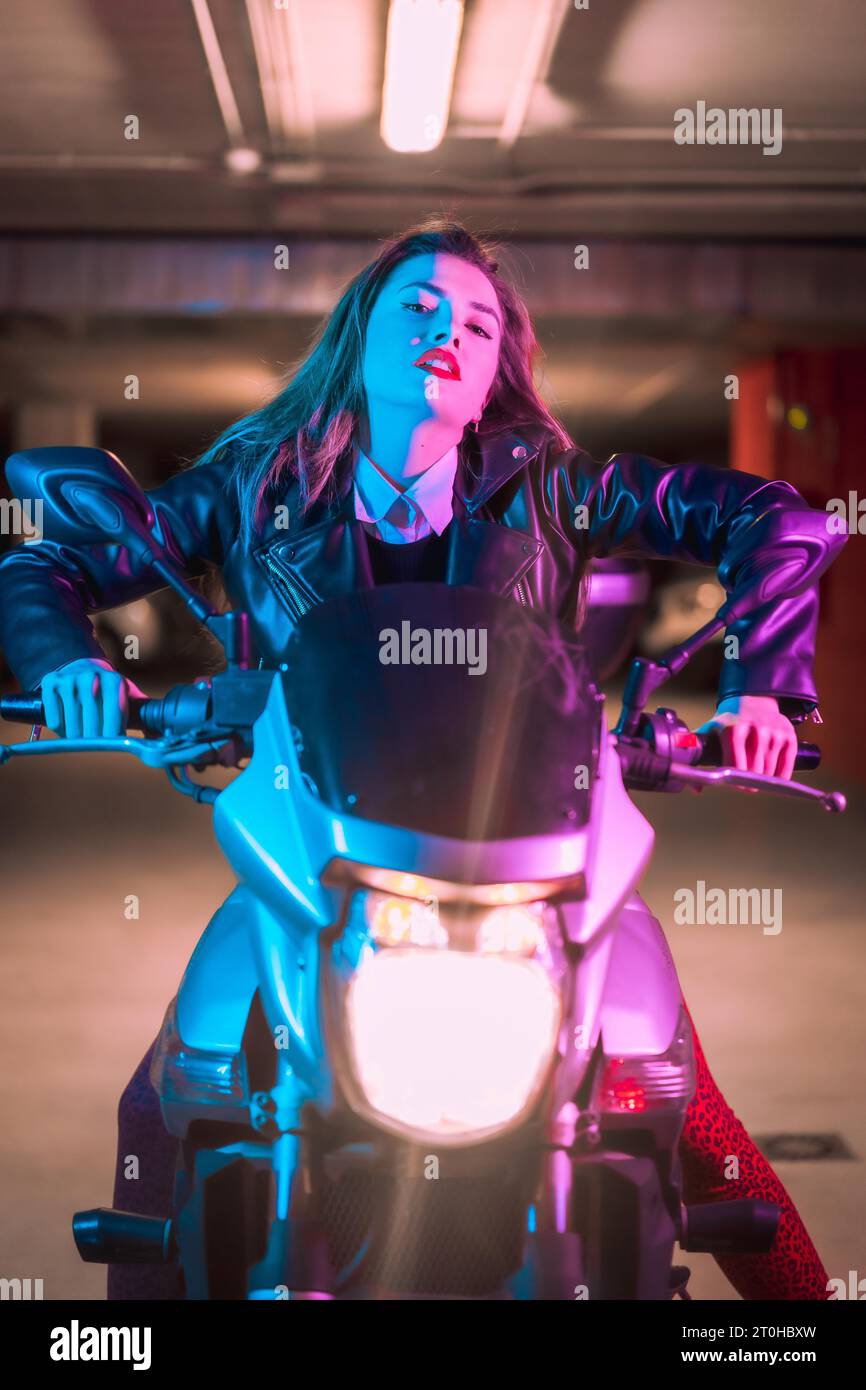 Photographie avec des néons bleus et roses sur une moto. Portrait d'un jeune modèle blond caucasien portant une veste en cuir noir Banque D'Images