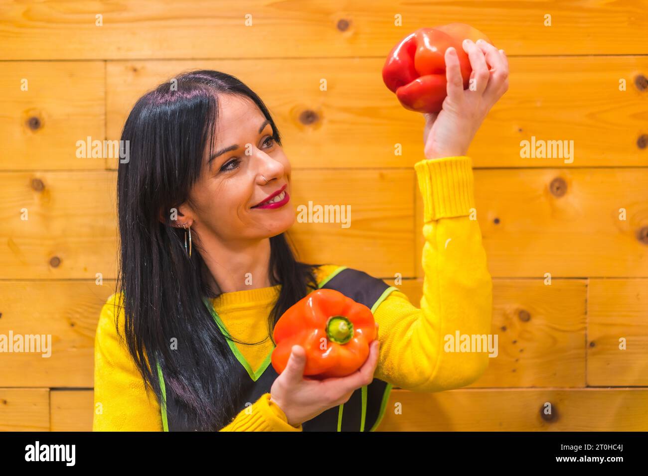 Poivrons rouges dans la main d'une brune fille fruitière caucasienne, travaillant dans un établissement de greengrocer Banque D'Images