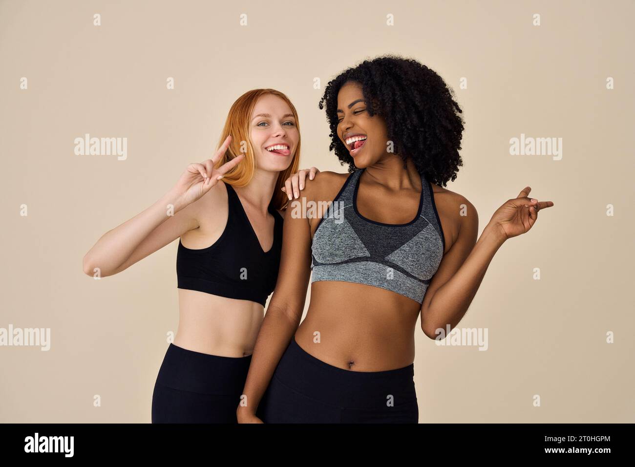 Deux filles heureuses assez diverses portant des vêtements de sport s'amusant sur fond beige. Banque D'Images