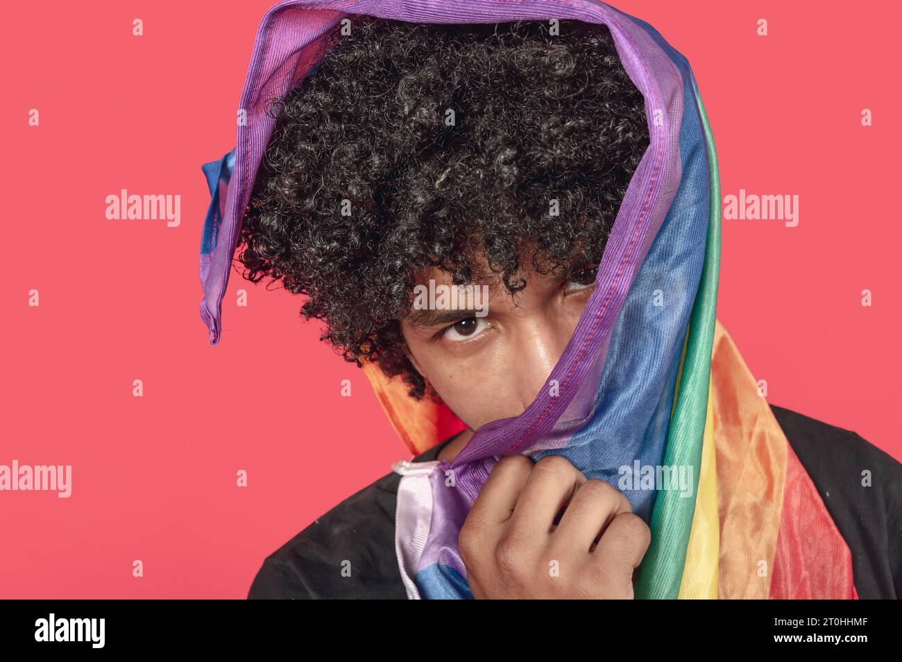 brunette jeune homme avec un drapeau LGBT au-dessus de la tête regardant la caméra, vue portrait Banque D'Images