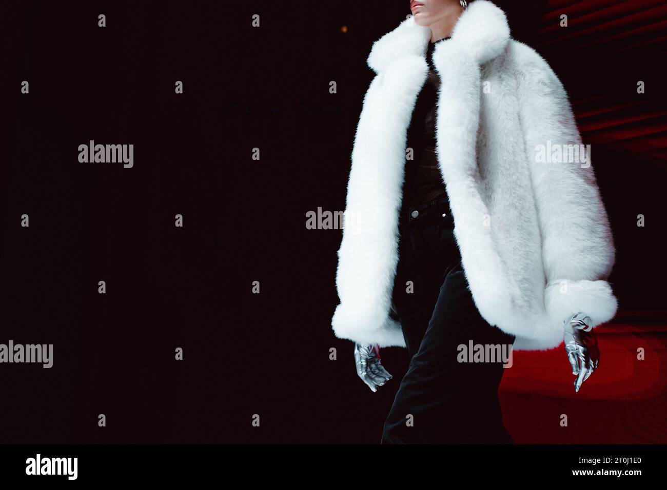 Détails de mode d'un manteau blanc pelucheux en fourrure d'hiver et gants argentés. Modèle de mode marchant sur fond noir Banque D'Images