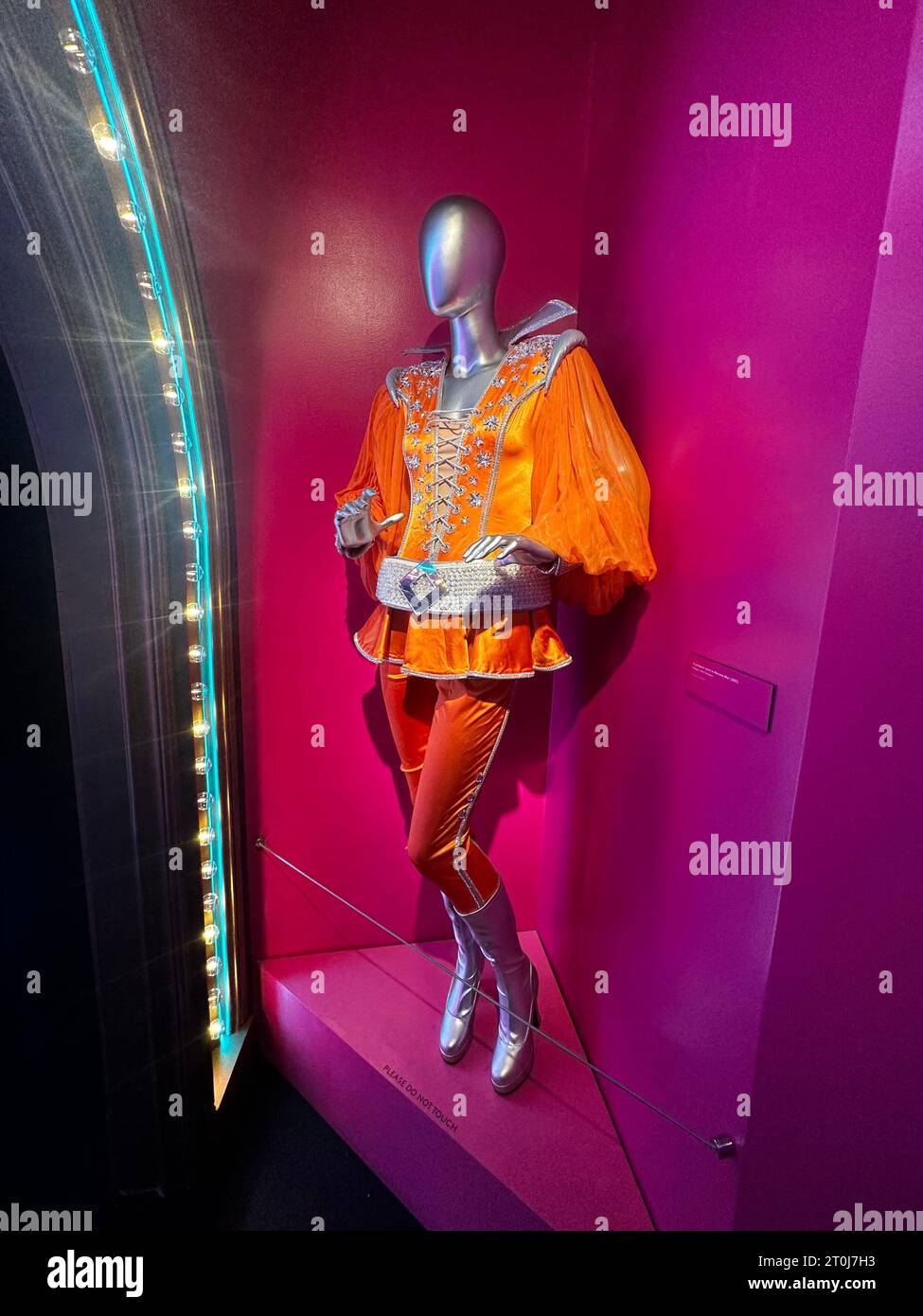 Costume musical Mamma Mia orange vif avec style disco des années 70 et bottes à plateforme, mettant en valeur la mode scénique vibrante et le design emblématique inspiré d'ABBA Banque D'Images