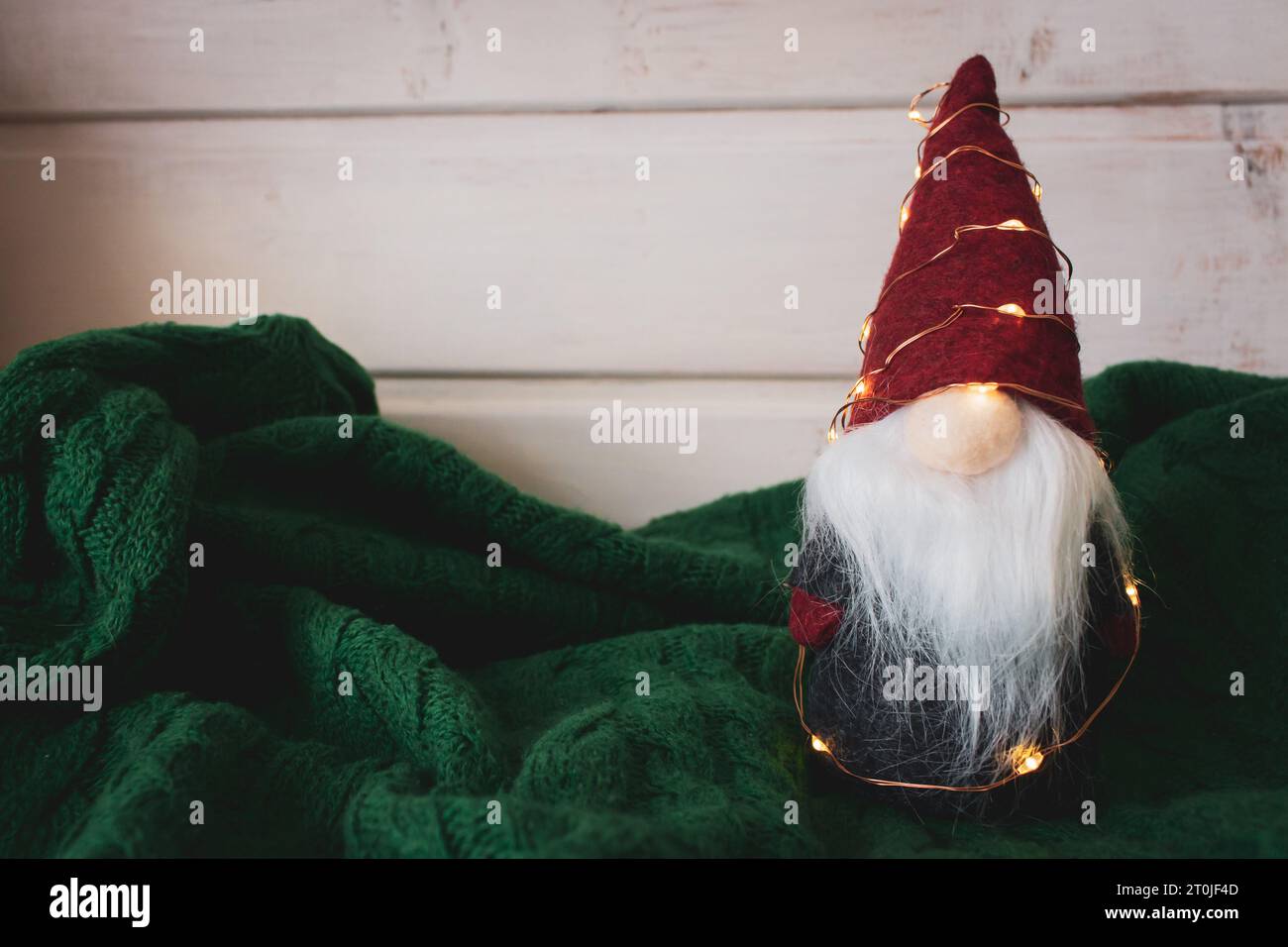 Jouet du Père Noël avec guirlande sur fond tricoté vert. Mignon nain avec chapeau conique rouge dans un design scandinave. Décoration de Noël. Ambiance de Noël Banque D'Images