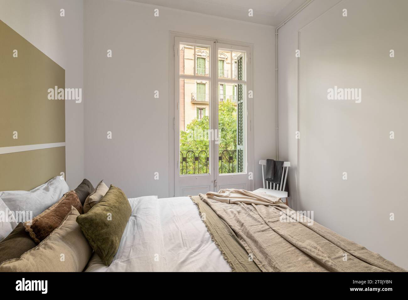 Magnifique vue sur le jardin d'été depuis la fenêtre de la chambre d'hôtel avec un lit double et des draps beiges dans un hôtel lune de miel. Le concept d'une pièce vide dans le Banque D'Images