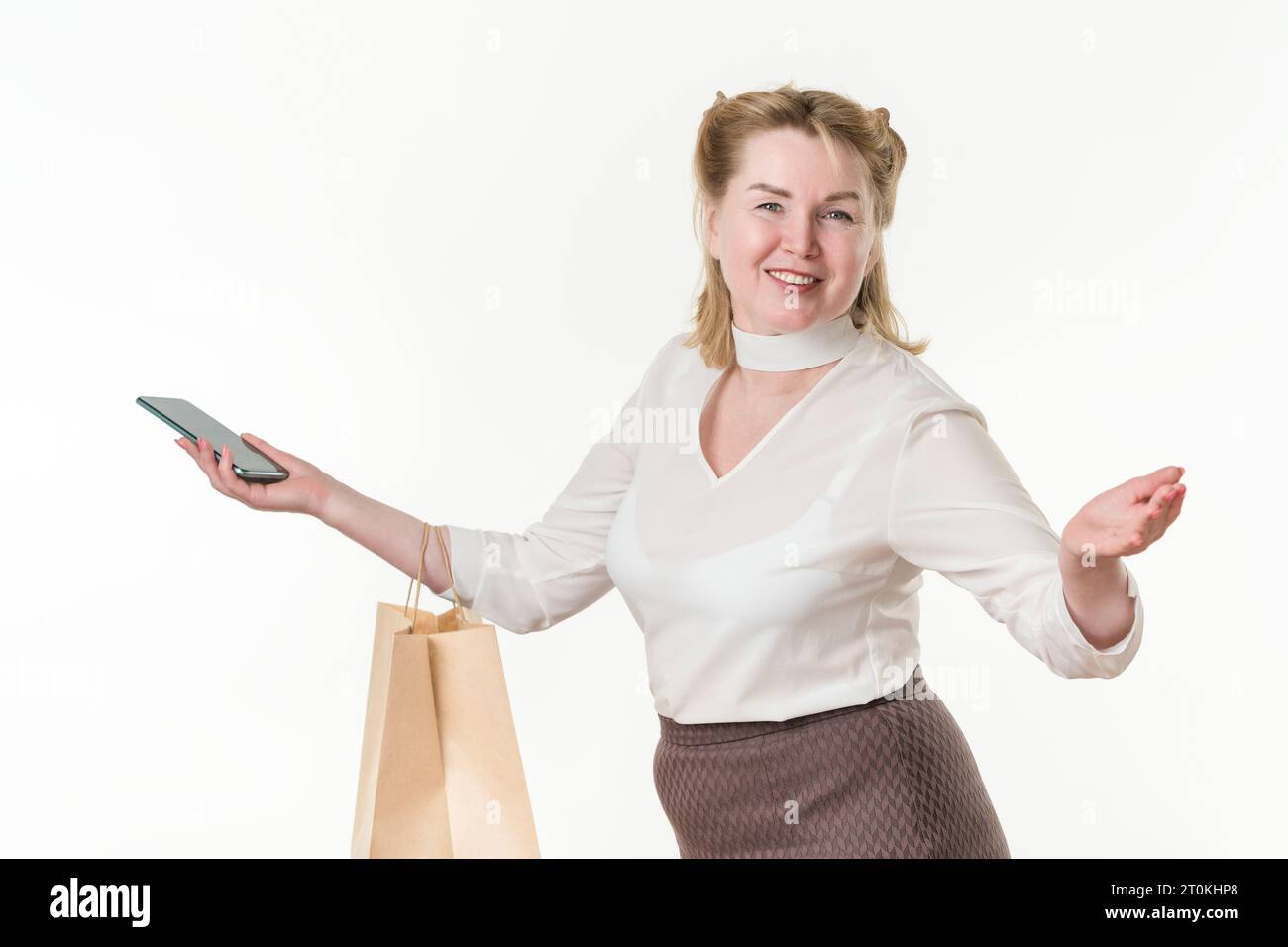 Taille vers le haut photo de femme heureuse avec sacs de paquet de papier d'achat et téléphone portable. Ethnicité caucasienne blonde femelle 49 ans souriant et regardant Banque D'Images