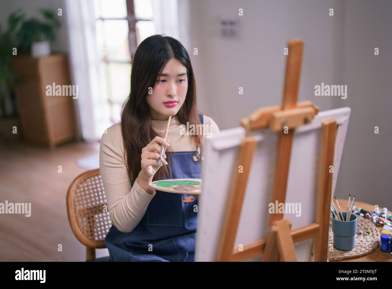 Jeune artiste féminine asiatique assise devant la toile et pensée idée à dessiner et peindre des œuvres d'art. Banque D'Images