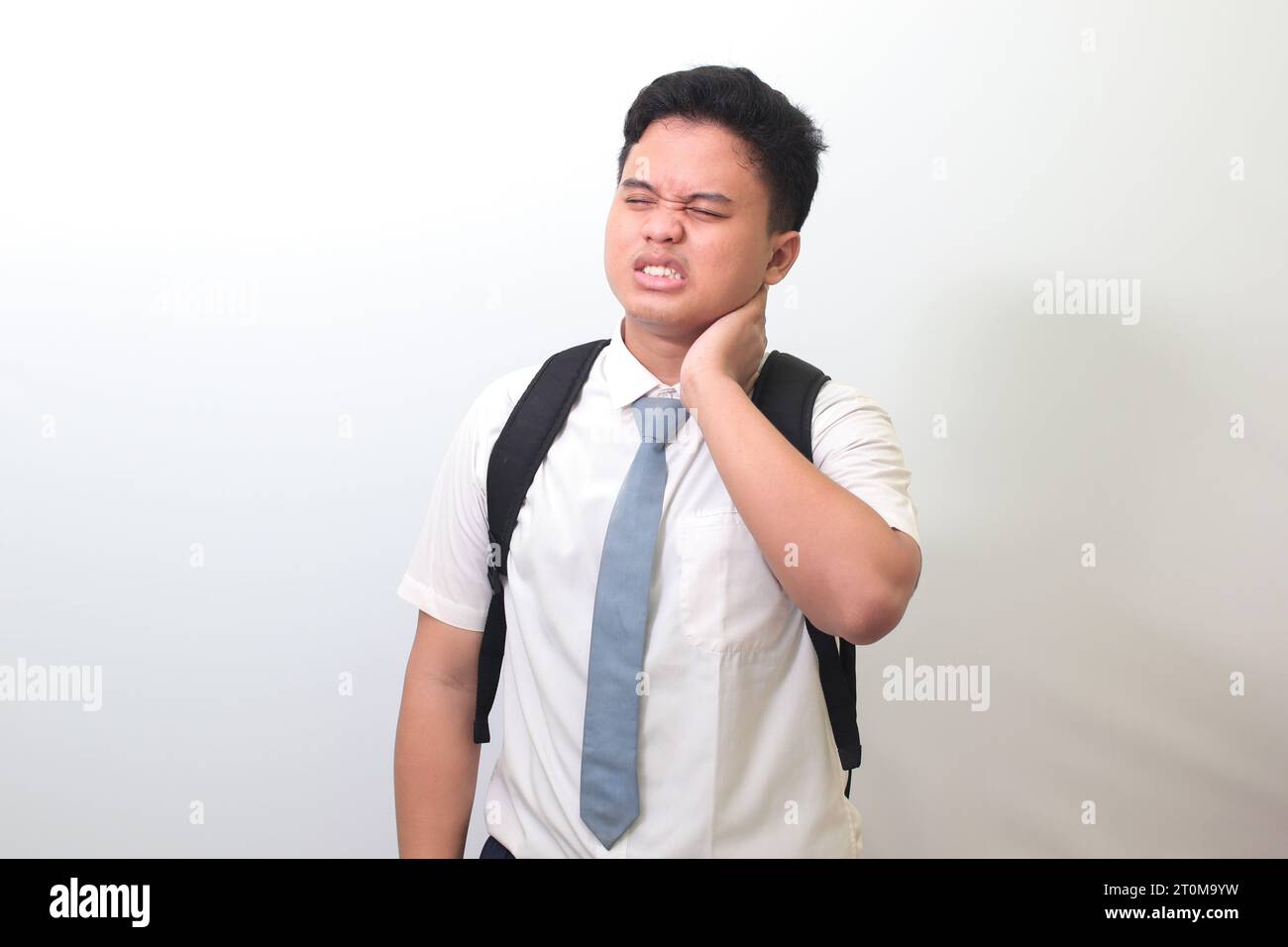 Lycéen indonésien portant un uniforme de chemise blanche avec une cravate grise touchant son cou et exprimant la négativité. Image isolée sur blanc b Banque D'Images