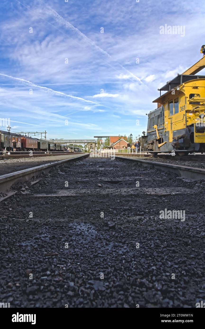 Voie ferrée du musée à faible angle de vue avec des restes de charbon et de suie. Sur la voie d'évitement une locomotive grue Sik diesel-électrique et un train avec de vieux wagons et des personnes Banque D'Images