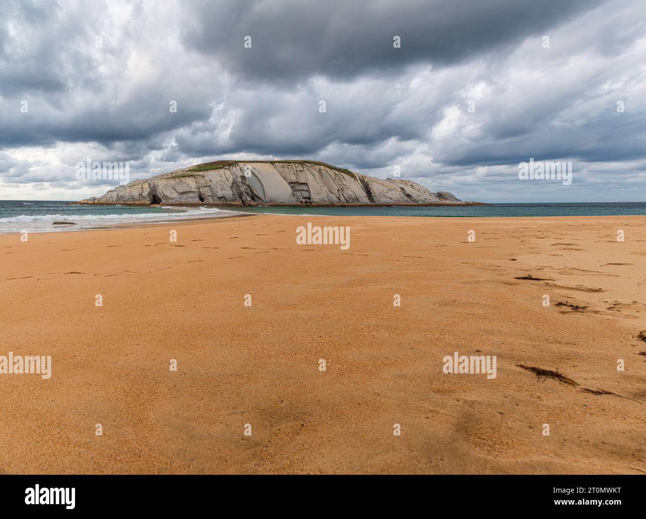 Vue panoramique de Isla del Castro avec plage de sable de Covachos, Santander, Cantabrie, Espagne. Île rocheuse et broche sablonneuse par jour nuageux de mauvaise humeur Banque D'Images