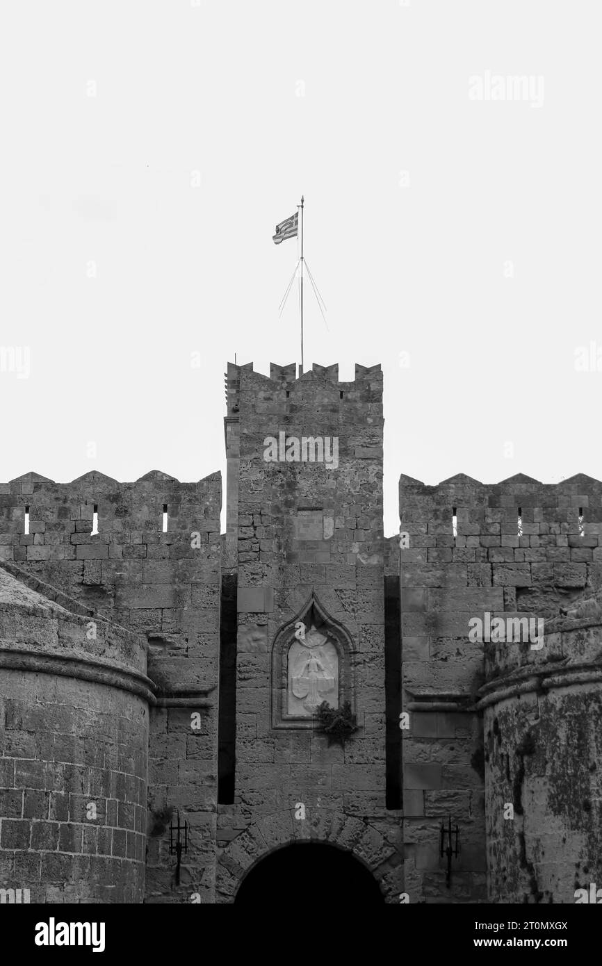 Gros plan noir et blanc de la porte d'Amboise situé dans le coin nord-ouest de la ville médiévale de Rhodes avec drapeau national de la Grèce sur le dessus Banque D'Images