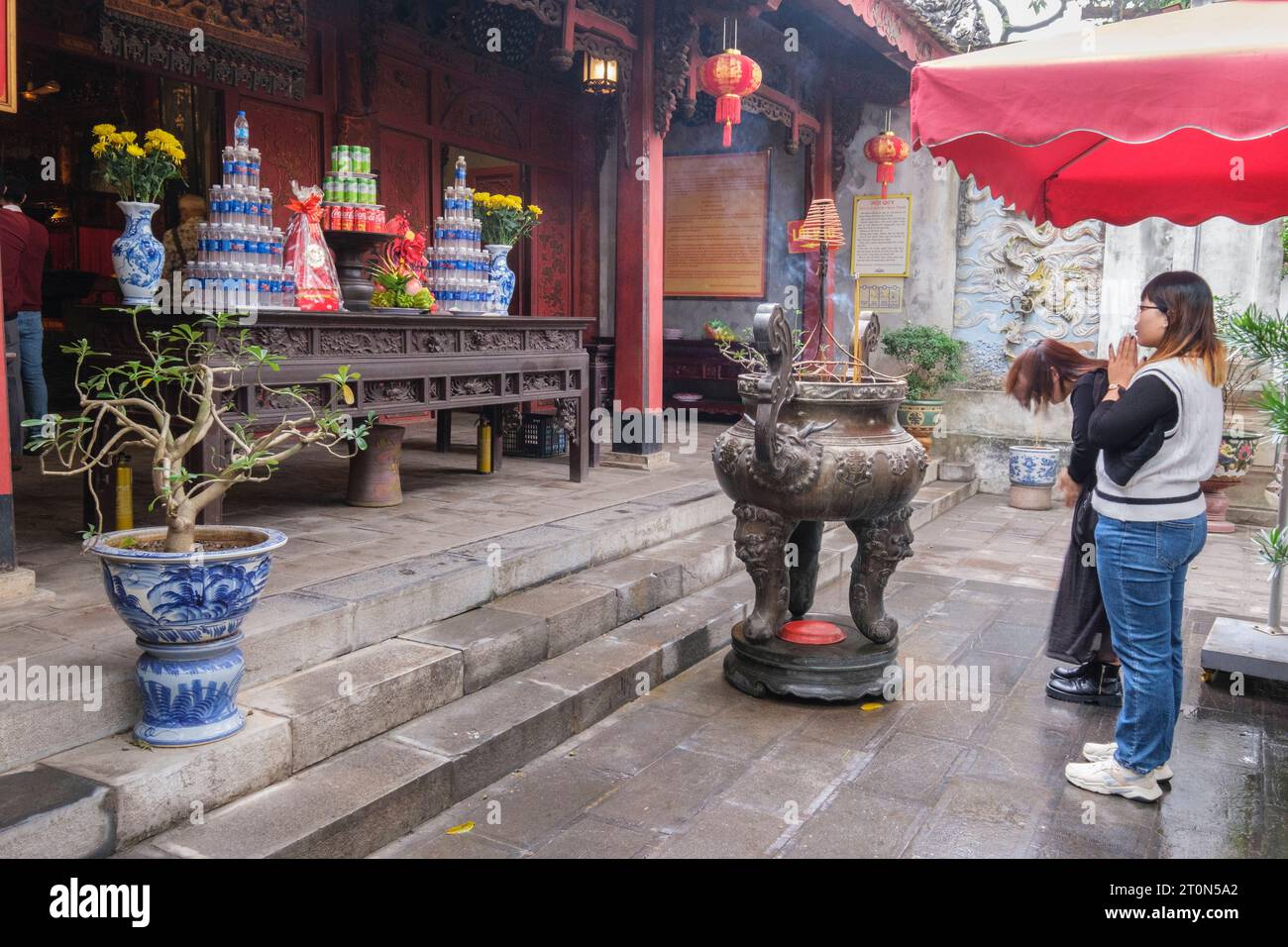 Hanoi, Vietnam. Temple Quan Thanh, un temple taoïste. Jeunes femmes priant devant des offrandes à l'entrée du Temple. Banque D'Images