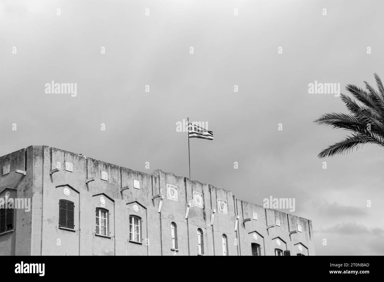 Drapeau national de la Grèce sur le dessus un bâtiment d'architecture européenne à Rhodes, Grèce en noir et blanc Banque D'Images