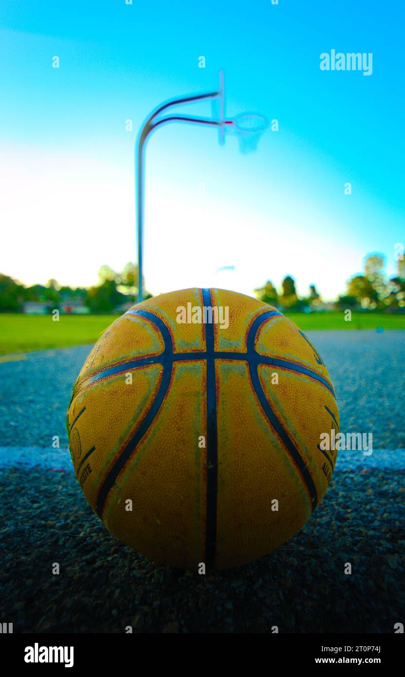 Un panier et un panier de basket-ball de terrain de jeu se dressent contre un ciel spectaculaire au lever ou au coucher du soleil. L'image transmet de multiples thèmes, tels que l'intemporalité des sports pour les jeunes, l'importance du sport dans la culture occidentale, la poursuite solitaire de l'excellence sportive Banque D'Images