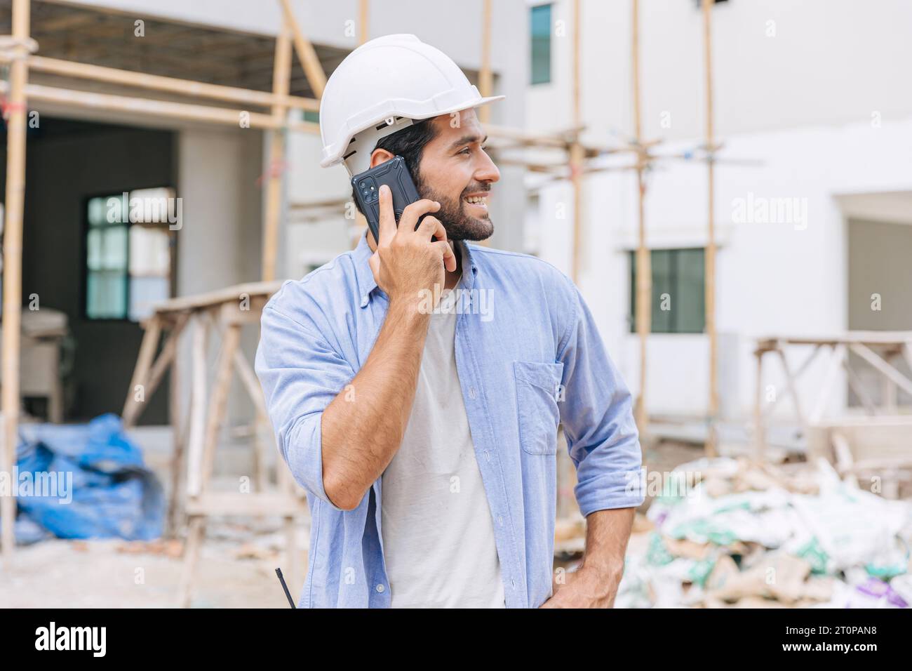 heureux contremaître constructeur utilisant le téléphone intelligent appelant le contact d'affaires dans le chantier de construction. ingénieur en construction ou architecte avec technologie de connexion moderne Banque D'Images